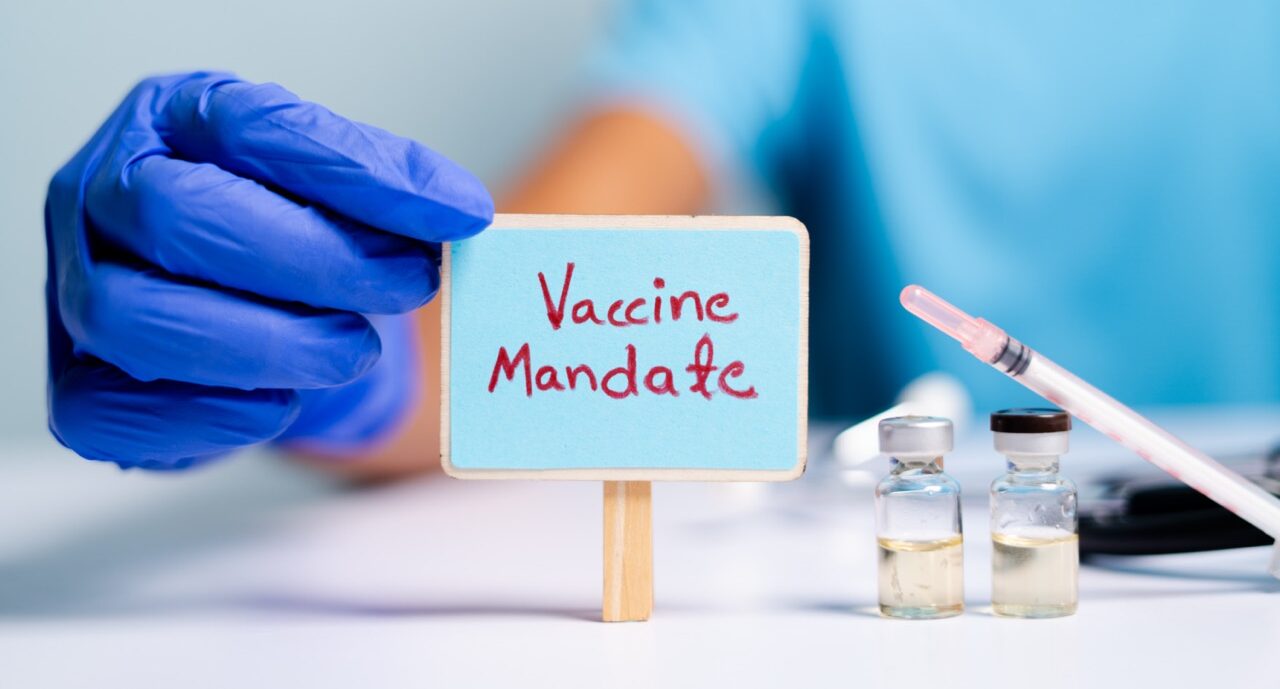 Concept of coronavirus or covid-19 vaccine mandate, showing with doctor hands with gloves by placing sign board next to vaccine shots and syringe.